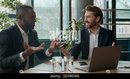 Two diverse businessmen business team happy discuss good online news ecxited men Caucasian man African American businessman with laptop in office Stock Photo