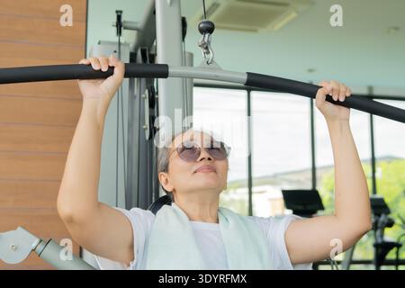 Happy senior Asian woman doing exercises in gym to stay fit. Sporty mature woman training in gym. Senior sport concept. Stock Photo