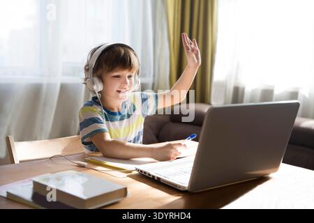child boy in earphones is using a laptop and study online at home. homeschooling, distant learning || Model released Stock Photo