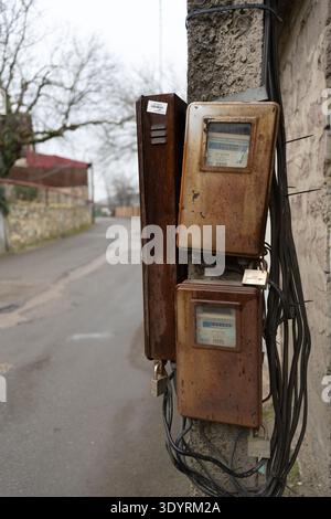 Old rusty electrical boxes mounted on a wall with exposed cables in rural area. Stock Photo