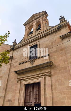 View of the grand, weathered stone facade of a historic building with dark wooden doors under a cloudy sky, Salamanca, Castile and León, Spain. Stock Photo