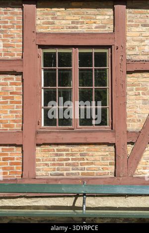 View of the window reflecting sunlight, framed by dark wood against a brick wall, casting shadows on a green bench, Oslo, Oslo, Norway. Stock Photo