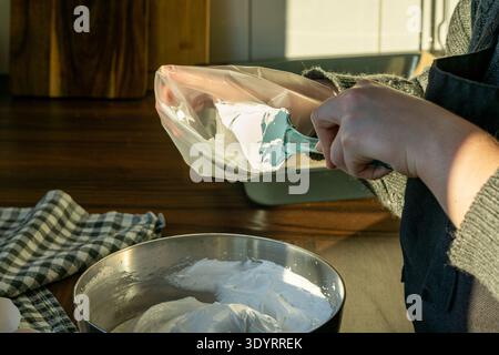 Person transfers whipped meringue from a metal bowl into a piping bag using a silicone spatula. Stock Photo