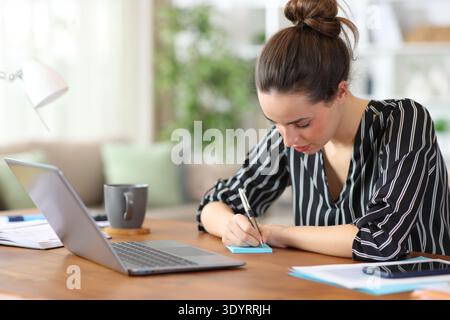 Serious freelance worker writing in sticky note on a wooden table working at home Stock Photo