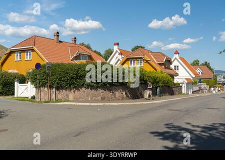 View of vibrant yellow and white houses with striking orange roofs peek over lush green hedges under a bright blue sky, in Bygdoy, Oslo, Norway. Stock Photo