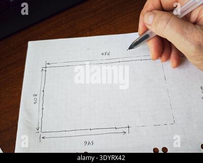 Kirov, Russia - February 11, 2026: A person is using a pen to outline a rectangle on a sheet of paper. The paper is placed on a wooden desk. Measureme Stock Photo