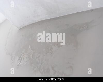 A close-up view of a textured wall with a light gray surface and a white corner. The wall shows signs of wear and unevenness. Stock Photo