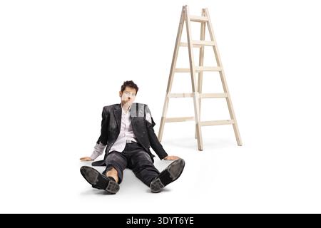Man in a ruined suit sitting on the floor next to a ladder isolated on white background Stock Photo