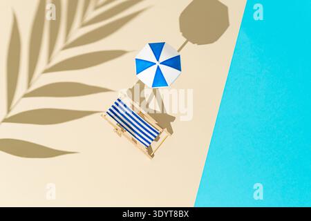 Mini beach deck chair with beach umbrella near pool on beige background with tropical palm shadow. Summer vacation concept. Flat lay style. Top view. Stock Photo