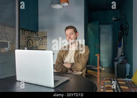 Man lying in bed working on laptop while resting with focused expression suggests concentration as he types and looks at the screen. Working from bed Stock Photo