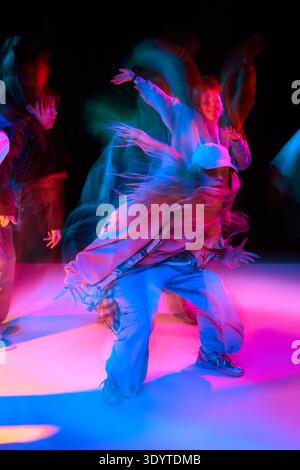 Female street dancer performing hip hop move with neon light trails and motion blur. Stock Photo