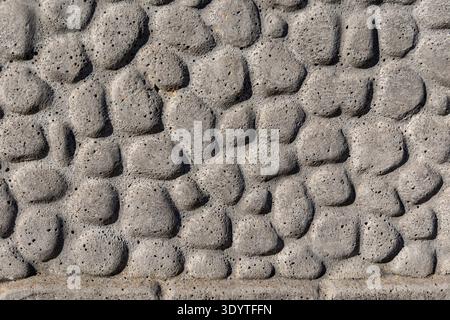 Gray Stone Wall Texture Background Closeup. Close-up of a rough gray stone wall surface with raised irregular shapes, porous texture, and natural Stock Photo