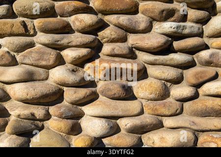 Sunlit River Stone Wall Texture Background. Close-up of a rustic wall built from rounded river stones in warm earthy tones, showing natural texture Stock Photo