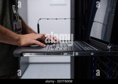 Data center technician typing on rack laptop while monitoring servers in a server room Stock Photo