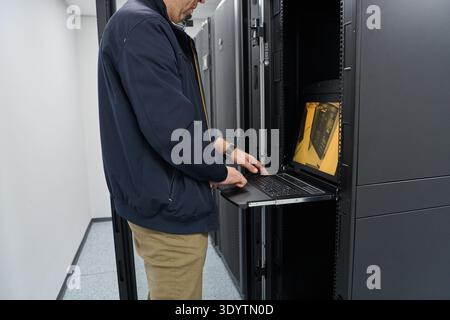 IT technician working on server rack console in a data center performing maintenance and monitoring Stock Photo