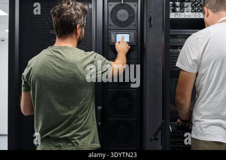 Two technicians working on server racks in a data center performing maintenance and system monitoring Stock Photo