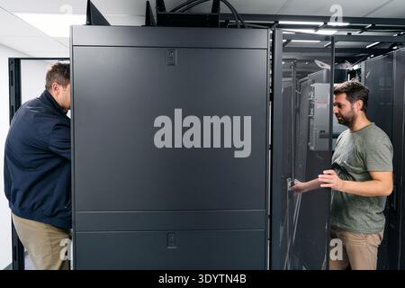 Two IT technicians working on server racks in a data center performing maintenance and hardware checks Stock Photo