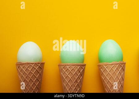 Green easter eggs in waffle cones on yellow background Stock Photo