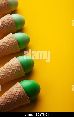 Green easter eggs in waffle cones on yellow background Stock Photo
