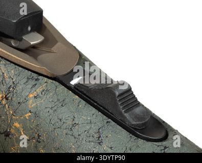 Tang-mounted safety on a rifle with a green stock and splatters of gold and black paint seen up close and back in the safe position. Stock Photo