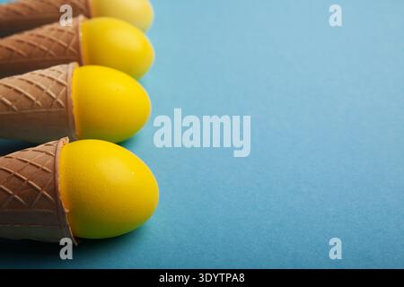 Yellow easter eggs in waffle cones on blue background Stock Photo