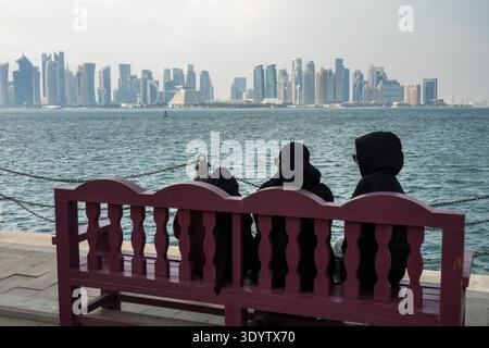 Doha skyline with women on bench wearing burqas viewed from Mina district, Doha, Qatar Stock Photo