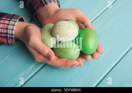 Woman holding green colored easter eggs on blue wooden planks Stock Photo