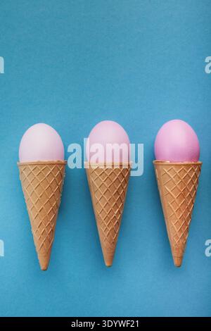 Pink easter eggs in waffle cones on blue background Stock Photo