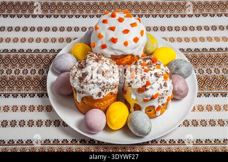 A celebratory spread of decorated Easter bread and colorful eggs presented on a white plate atop a traditional Ukrainian rushnyk Stock Photo