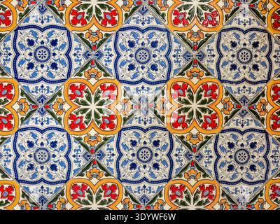 A detailed close up of traditional Portuguese azulejo tiles featuring a repeating pattern of blue, red, and yellow floral motifs on a white background Stock Photo