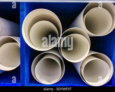 A close up abstract perspective of several white PVC pipes neatly arranged and stacked within a vibrant blue storage compartment, showcasing circular Stock Photo