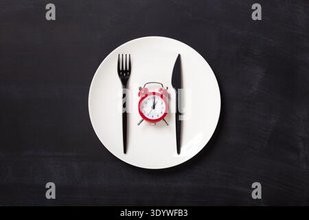 Top view on plastic forks and clock on white plate at black background Stock Photo