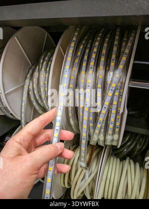 A person's hand selects a flexible LED strip light from a shelf filled with spools of lighting elements Stock Photo
