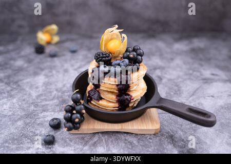 Pancake tower with berries and honey drizzle served on skillet in rustic breakfast setup Stock Photo