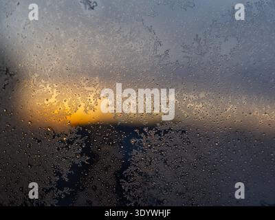 Abstract winter background featuring frozen water drops and ice flowers on glass at dusk. Stock Photo