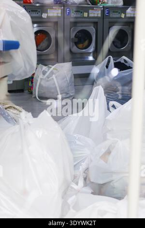 Self service laundromat with washing machines and bags of laundry waiting to be washed. Everyday life concept. Stock Photo