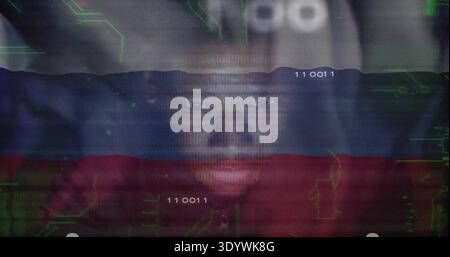 Leaning man in red shirt and dark hood responding to screen glow at workstation, reading binary Stock Photo