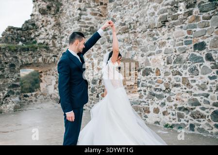 Bride and groom dancing, looking at each other. Wedding couple standing outside near ruins. Stock Photo