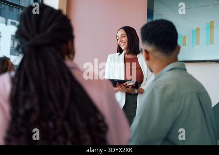 Smiling businesswoman holding tablet and presenting to team during meeting in boardroom at office Stock Photo