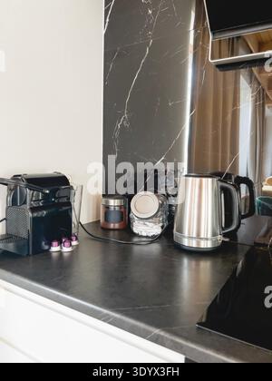 Modern coffee station with black capsule coffee machine, metal kettle and glass jars on dark marble countertop, minimalist hotel style kitchen. High q Stock Photo