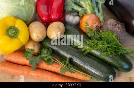 Assorted fresh vegetables on wooden cutting board including carrots, zucchini, potatoes, cabbage, beetroot, bell peppers, onion, garlic, broccoli and Stock Photo