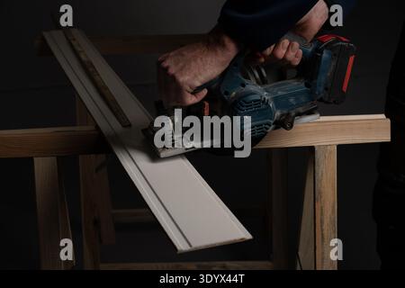 Close up of worker using handheld circular saw to cut wooden board on workbench. Carpentry and woodworking concept with power tool during DIY home imp Stock Photo