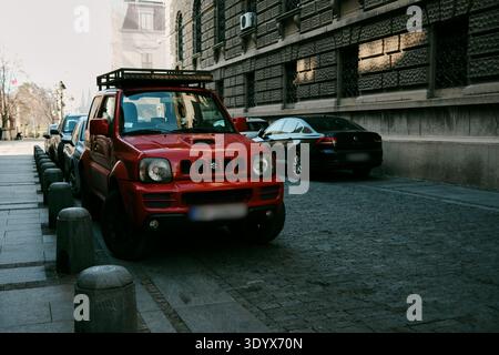 Red Suzuki Jimny parked along a cobblestone street beside historic stone architecture in central Belgrade. Belgrade, Serbia - March 9, 2025. Stock Photo