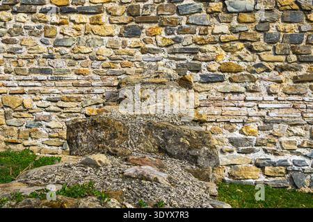 Weathered stone wall built from irregular rocks with remains of an old structure in front, showing detailed masonry texture at a historical architectu Stock Photo