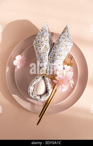 Easter Table Setting with Bunny Napkin and Decorated Egg.  Festive Spring Arrangement on Pink Background Stock Photo
