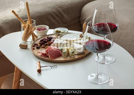 Elegant charcuterie board composition featuring assorted cheeses, cured meats, walnuts, dried cranberries, breadsticks, olives, and red jelly, paired Stock Photo