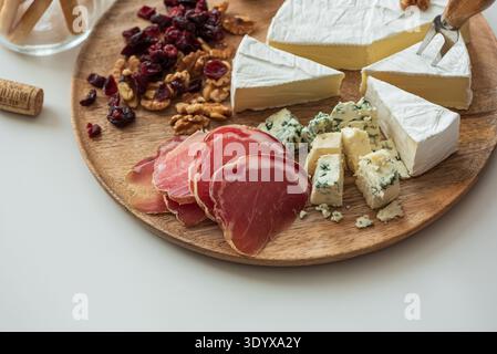 Elegant charcuterie board composition featuring assorted cheeses, cured meats, walnuts, dried cranberries, breadsticks, olives, and red jelly, paired Stock Photo