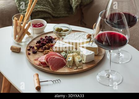 Elegant charcuterie board composition featuring assorted cheeses, cured meats, walnuts, dried cranberries, breadsticks, olives, and red jelly, paired Stock Photo