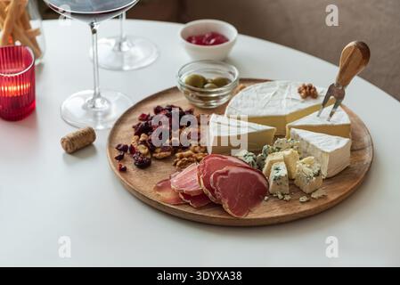 Elegant charcuterie board composition featuring assorted cheeses, cured meats, walnuts, dried cranberries, breadsticks, olives, and red jelly, paired Stock Photo