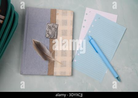 Notebook, pen, notepaper sheets and pen case on pale turquoise surface. High angle view. Stock Photo